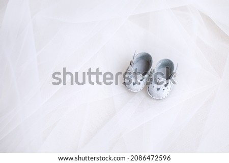White miniature shoes for a doll made of genuine leather on white organza. Beautiful shoes with a picture of a heart. Horizontal photo of clothing items with place for text.