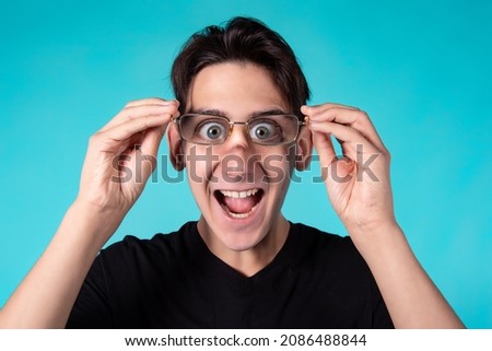 A funny man with glasses makes grimaces at the camera. Portrait of a guy against a blue background.