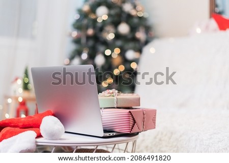 Christmas gift boxes or presents on laptop, online shopping concept. Glowing snow bokeh with Christmas tree. Winter holidays on white background with empty space for text.
