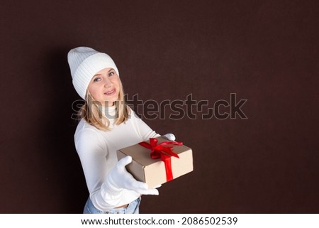 Woman with a gift in her hands on a dark background. Young woman in white hat and gloves