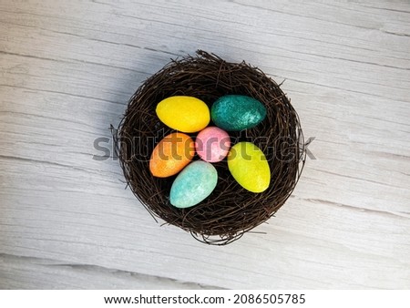 Colorful Easter Egg Nest with Extra White or Gray Wood Board Background for room or space for copy, text, words. A flat lay with square crop, Happy Easter Holliday concept top view