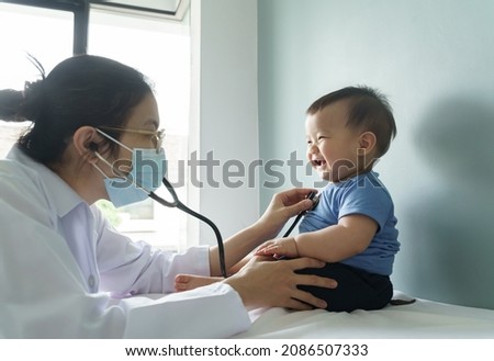 Asian female doctor wearing face mask examining little cute Baby boy with stethoscope in medical room at hospital. BeH3althy Royalty-Free Stock Photo #2086507333