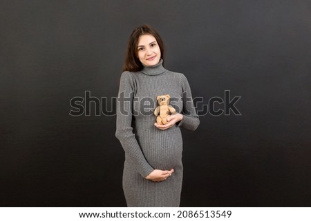 Happy pregnant woman holding a teddy bear against her belly at Colored background. Young mother is expecting a baby. Copy space.
