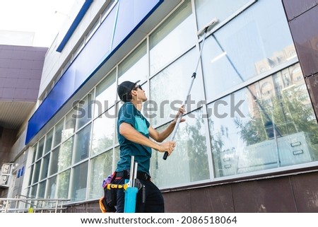 An employee of a professional cleaning service in overalls washes the facade and windows with special devices Royalty-Free Stock Photo #2086518064