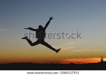 Silhouette of happy girl jumping playing on mountain at sunset or sunrise