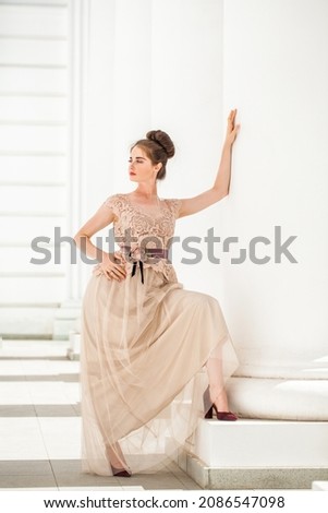Young beautiful brunette in a luxurious beige dress posing on the street