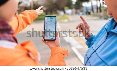A woman holds a smartphone with an online map and shows the way to an elderly woman with her hand. Mature woman was lost in the city. Close up. Concept of memory loss and dementia. Royalty-Free Stock Photo #2086547533