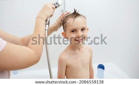 Young smiing boy looking in camera while mother washing his head in shower Royalty-Free Stock Photo #2086558138