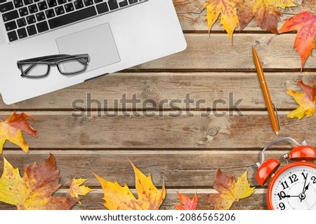 Office desktop with keyboard, alarm clock with autumn leaves