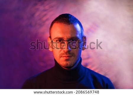 Neon portrait of serious man wearing glasses with black frame and dark turtleneck sweater on cosmic silver multicolored background