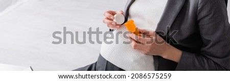 cropped view of pregnant woman holding jar with pills in office, banner