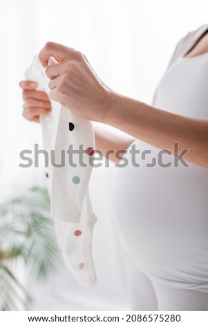 partial view of pregnant woman holding baby romper in bedroom