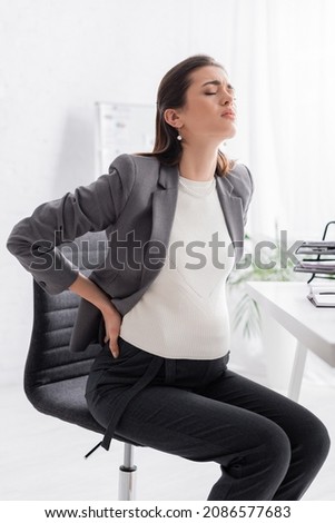 exhausted pregnant woman touching back in office