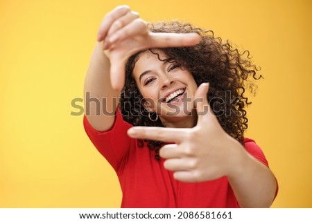Portrait of optimistic happy and creative female student imaging her new apartment as extending hands and showing frames gesture smiling through it at camera amused and carefree over yellow wall