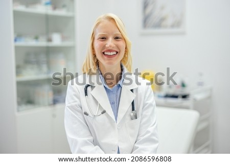 Happy blonde doctor, posing for the picture and smiling in her office.