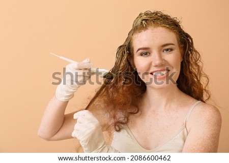 Young woman using henna hair dye on color background