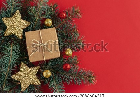 Gift box with spruce branches and christmas ornaments  on a red background. Holiday concept. Place for text. Flat lay.