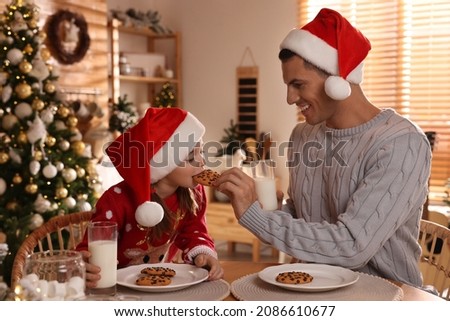 Happy father and his daughter eating delicious Christmas cookies at home
