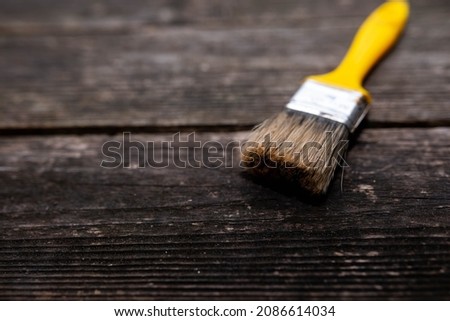 Used paintbrush with vibrant yellow plastic handle on aged pine wood boards, space for text.