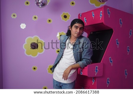 Beautiful hipster latino man in seductive pose next to vintage gaming machine. Romantic photo of non binary man lying on the carpet. Royalty-Free Stock Photo #2086617388