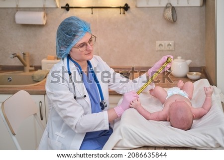 Doctor measures the growth of a newborn baby. A nurse in uniform checks the girth of the child head and abdomen