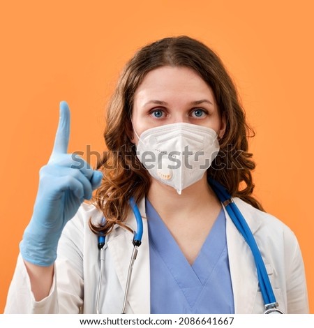 The doctor makes a careful finger - up gesture, copy space. A woman in medical protective gloves and a mask on a red background, concept