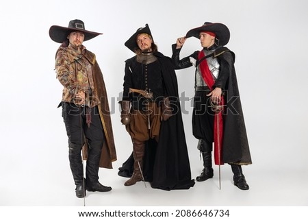 Portrait of thee men in vitage costumes with swords, musketeer and pirate isolated over white background. Combination of medeival and modern styles. Concept of history. Copyspace for ad.