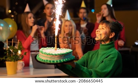 Beautiful Caucasian Female Holding a Cake as Her Co-Workers Cheer Her on In The Background Wearing Party Hats. Caucasian Office Workers Throwing a Surprise Birthday Party For Their Co-Worker. Royalty-Free Stock Photo #2086650445