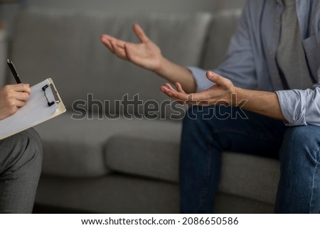 Unrecognizable man talking to psychotherapist at office, sitting on sofa and having consultation with counsellor, closeup view, cropped. Professional psychological help concept