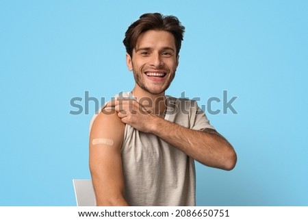 Covid-19 Vaccination. Excited Young Male Demonstrating Arm With Adhesive Bandage After Coronavirus Vaccine Shot, Portrait Of Vaccinated Millennial Man With Plaster On Hand Posing On Blue Background Royalty-Free Stock Photo #2086650751