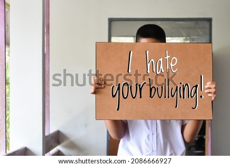 Asian boy holds brown paper which has texts " I hate your bullying" in front of the door, concept for calling all people around the world to stop bullying.