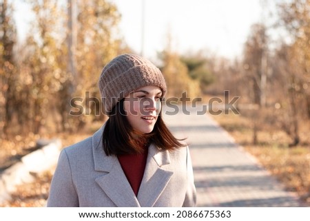 Smiling girl in a knitted hat and coat walks along the cobbled path of an autumn deserted park lake