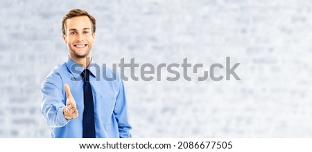 Businessman giving hand for handshake, over white brick loft wall background. Success in business, wellcome ad concept. Portrait of man in blue confident clothing. Male bank manager, executive.