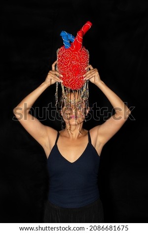 Young latin woman posing isolated holding a plush heart on black background. Female body expression concept