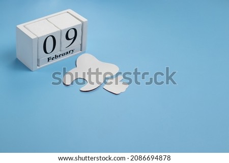 White paper cut tooth with cubic white calendar with date 9 February on light blue background. Banner for world dentist day with copy space.