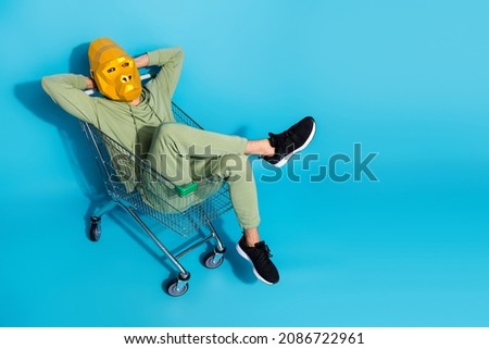 Photo of relaxing guy dressed animal mask sitting trolley arms behind head empty space isolated blue color background