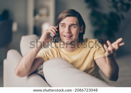 Photo of sociable friendly cheerful busy guy look up make phone call sit comfy divan wear yellow t-shirt home indoors