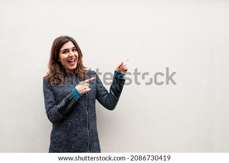 Woman with surprised excited face pointing something with finger to empty copy space isolated om white.