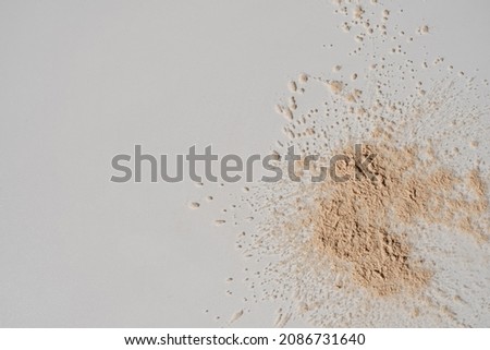 Beige cosmetic powder scattered on white background. Aesthetic beauty product concept. Flat lay, top view