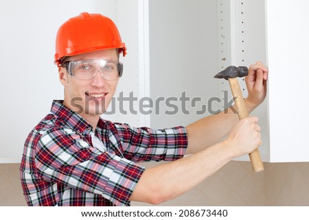repairman in a helmet with a hammer hits the nail