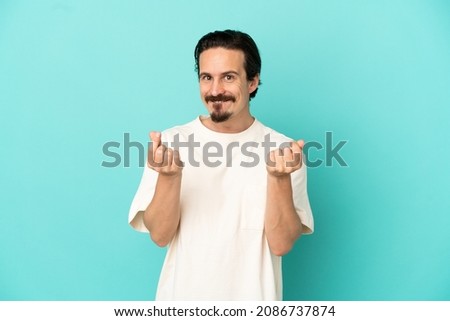 Young caucasian man isolated on blue background making money gesture