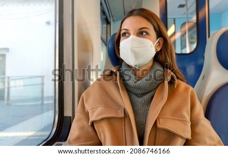 Travel safely on public transport. Young woman with KN95 FFP2 face mask looking through train window. Commuter passenger with protective mask travels sitting on train. Royalty-Free Stock Photo #2086746166