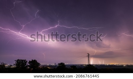 Long, branched, powerful lightning bolts strike down behind the trees. Dramatic lightning bolt. High quality photo