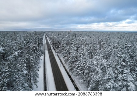 Aerial view of asphalt highway leading through frosty winter forests and groves covered with hoarfrost and snow. Drone photo of black road line and trees with chill snow in mountains. Christmas theme