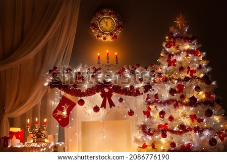 Christmas tree decorated with Lights in Fireplace Room with Candles, Red Stocking, Wreath and Clock on Wall. Shining White Xmas Tree at New Year Night Eve