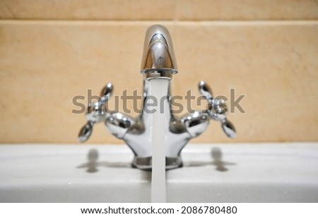 Common mixer tap. Water flowing out of bathroom stainless steel pillar tap into sink. Wasting water by leaving chrome faucet tap running. Overusing household water. Water misuse in domestic duties
