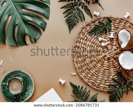 Natural flat lay with coffee cup, coconut, green monstera leaf on brown background. Space for text, blogger background, neutral colors, workspace