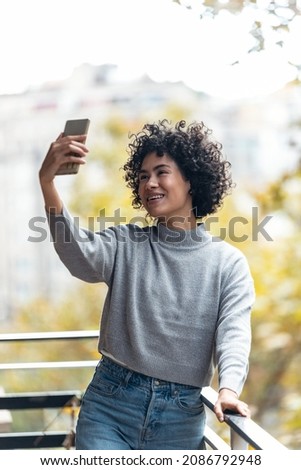 Shot of beautiful woman taking photos of herself with her smartphone while standing in the balcony at home.