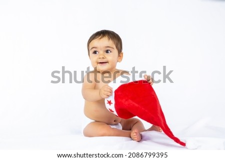 A baby boy with a red Christmas hat on a white background, copy space, taking off the Santa hat