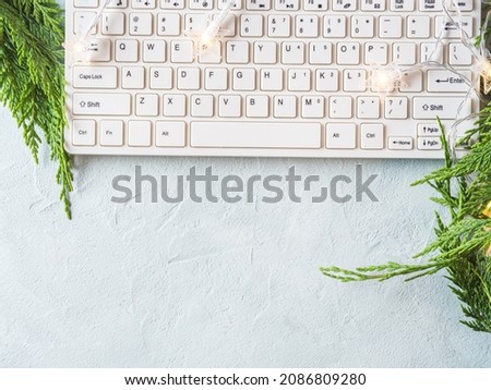 Workplace winter background with keyboard on gray background with green branches and star lights. Online blog, holiday shopping concept